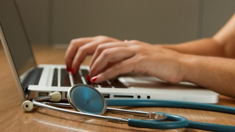 Typing on a laptop beside a stethoscope