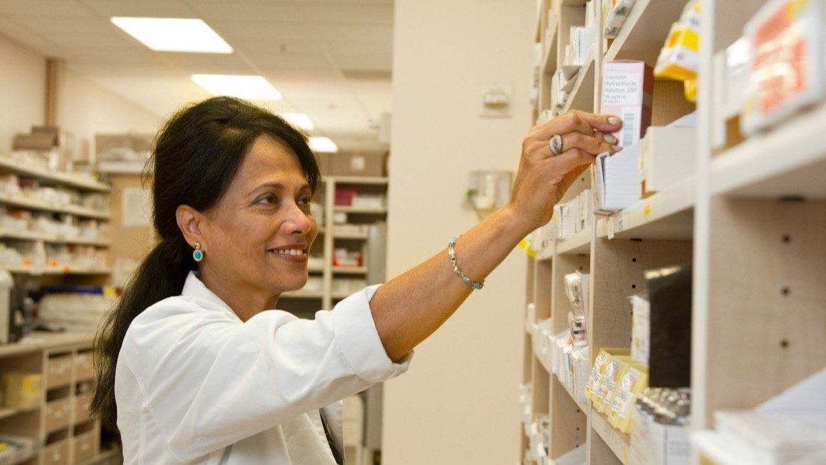 Pharmacy professional selecting a medication box from shelving